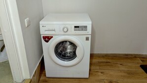 Un lave-linge à chargement frontal compact et blanc, de la marque LG, doté d’un moteur à entraînement direct et d’une capacité de 6 kg, avec un écran numérique, placé dans un coin d’une pièce au sol en bois et aux murs blancs.