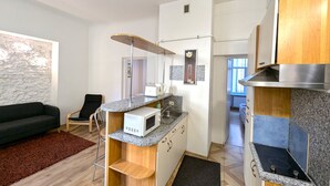 Une cuisine compacte équipée d’un four à micro-ondes, d’un évier et d’une cuisinière, ainsi qu’un canapé noir et une petite table en bois.