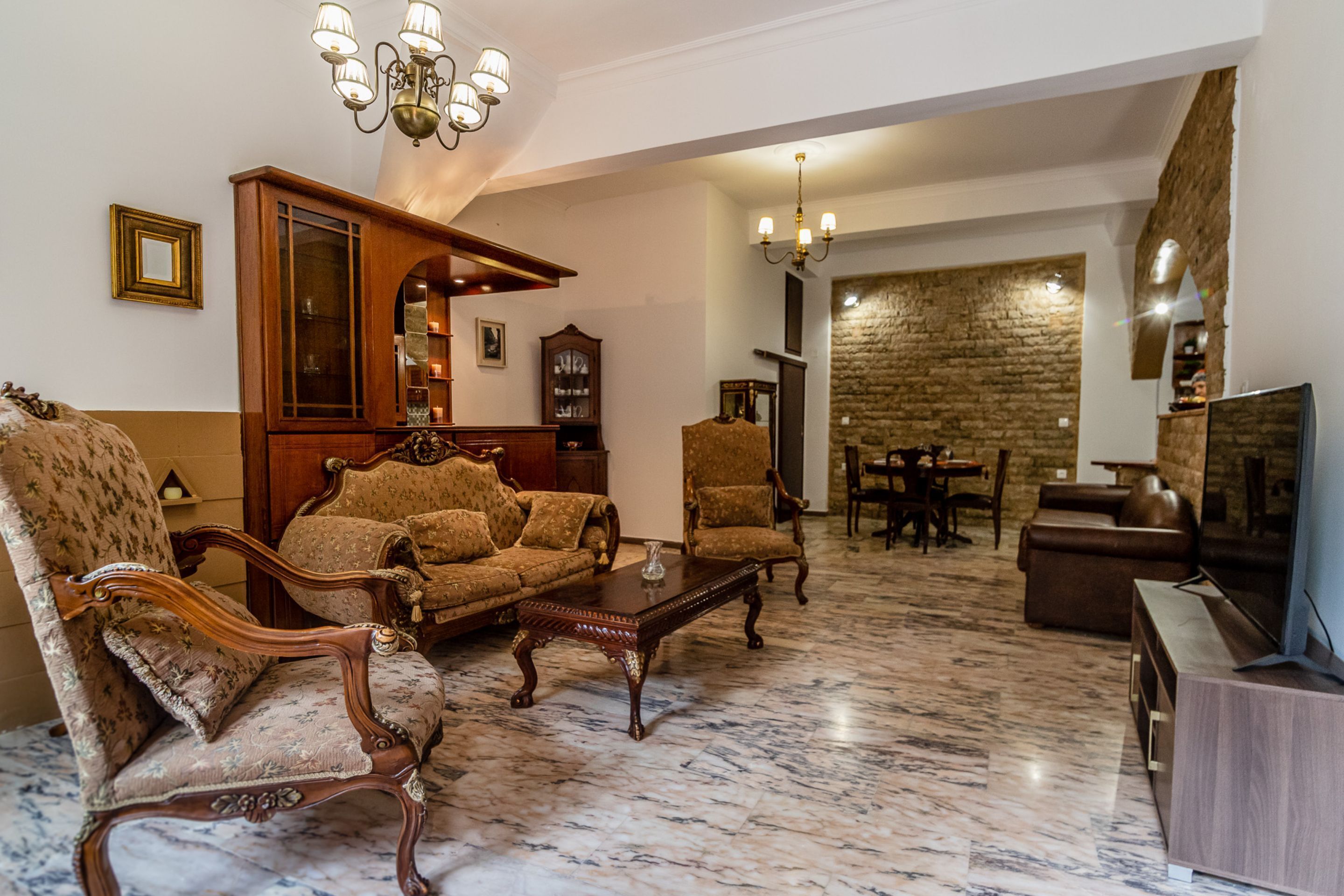 A spacious living room with a marble floor, wooden furniture, and a stone wall.