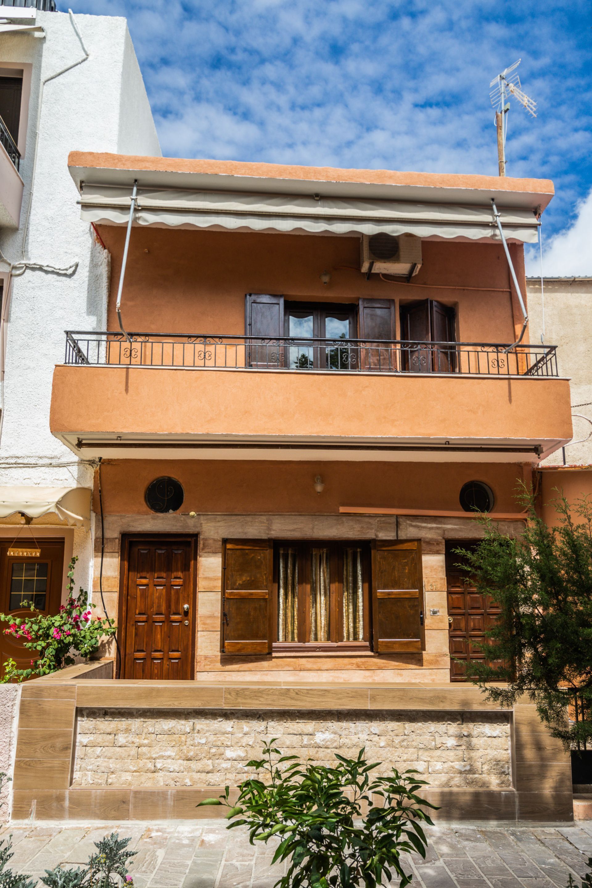A two-story building with a balcony, a stone entrance, and a visible door.