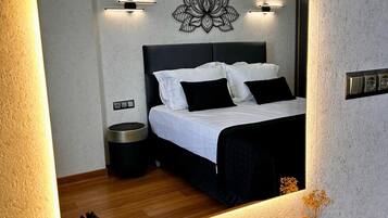 A modern bedroom with a large mirror reflecting the bed and wall decor, a bedside table with a vase, and a small potted plant.