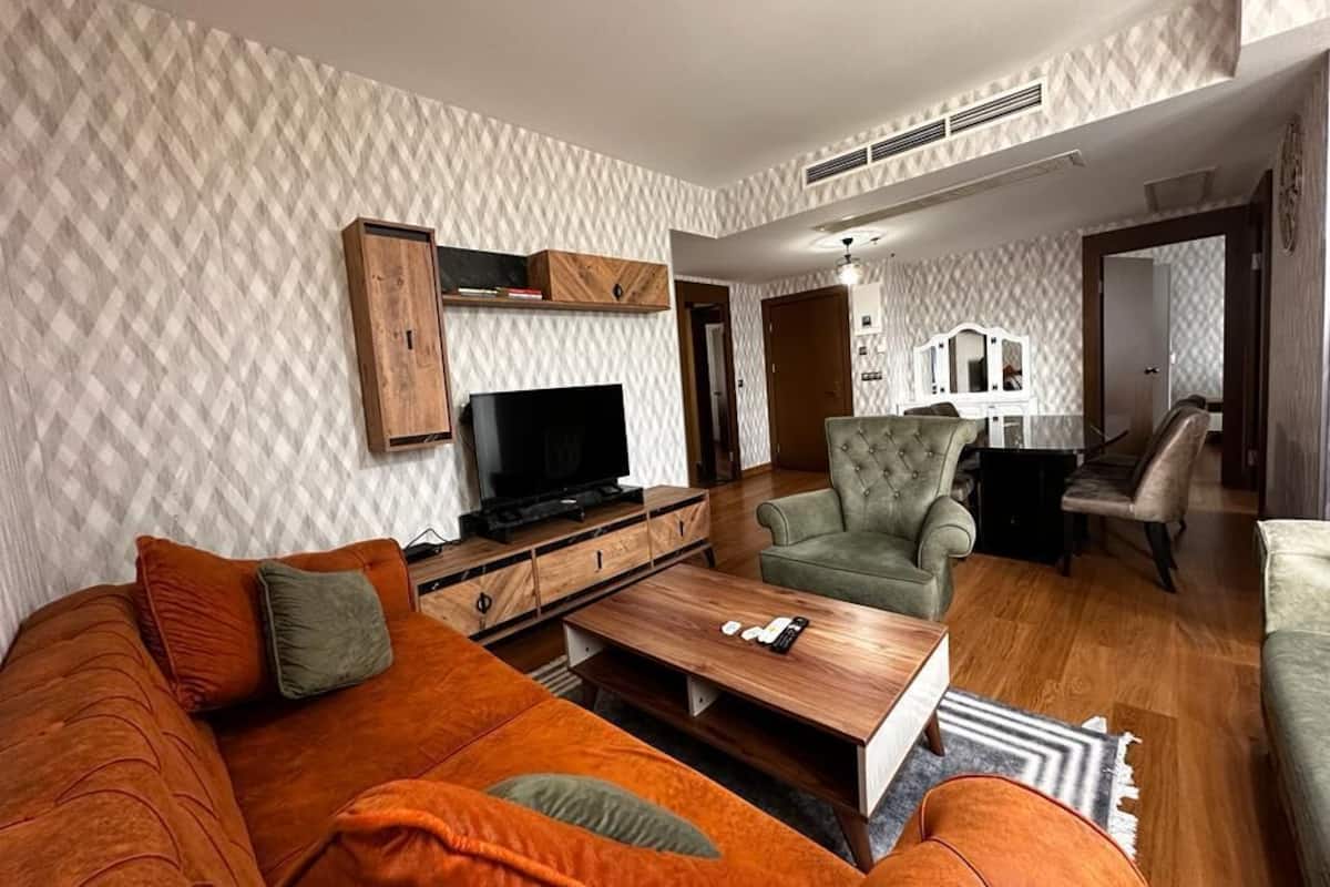 A living room with a sofa, armchair, and coffee table. There is a television and a cabinet.