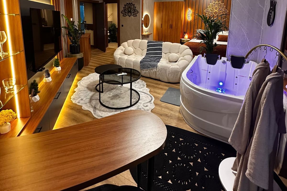 A modern hotel room with a wooden vanity, a round black table, a white sofa, a large bathtub, and a black decorative chair.