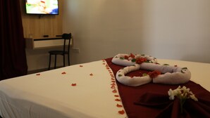 A hotel room with a bed covered in white sheets, a red blanket, and a bouquet of flowers. There is a TV mounted on the wall and a chair in the corner. - Hotel Mizwar Djerba (Houmt Souk)