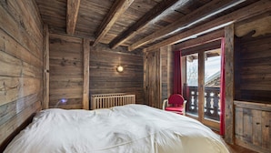 Habitación tipo cabaña de madera con una cama, una silla roja y una ventana que ofrece vistas al exterior.