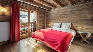 Un dormitorio de cabaña de madera con una cama, cortinas rojas y vistas a un paisaje nevado a través de un ventanal.