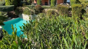 Ein zweistöckiges Haus mit Swimmingpool, umgeben von üppiger Vegetation und Hügeln im Hintergrund.