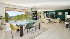 Ein modernes Wohnzimmer mit einem Glastisch, bequemen Sitzgelegenheiten, einem Fernseher und Blick ins Freie.