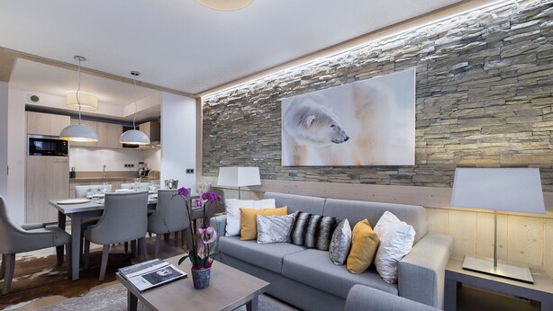 Un salon moderne avec un canapé gris, une table basse sur laquelle se trouve un ordinateur portable, et un coin repas avec des chaises et une table.