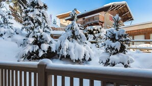 Un espace extérieur enneigé, doté de rampes en bois, d’arbres chargés de neige et d’un bâtiment à la façade et au balcon en bois.