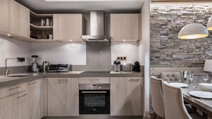 Une cuisine moderne avec des meubles de couleur bois clair, un four encastré et un mur de pierre en guise de crédence.