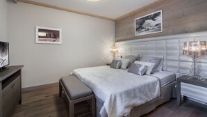 Une chambre à coucher comprenant un lit, des tables de chevet, un banc, un téléviseur et un luminaire au plafond.