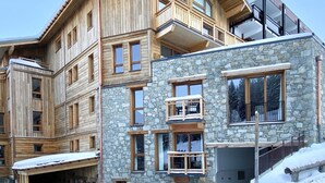 A multi-story building with wooden and stone facades, large windows, and balconies. - Beautiful apartment in Courchevel with parking 300m from slopes (Courchevel 1550)