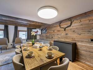 A dining area with a wooden table set for four, surrounded by chairs. A television is mounted on the wall, and there is a window with curtains. - Beautiful apartment in Courchevel with parking 300m from slopes (Courchevel 1550)
