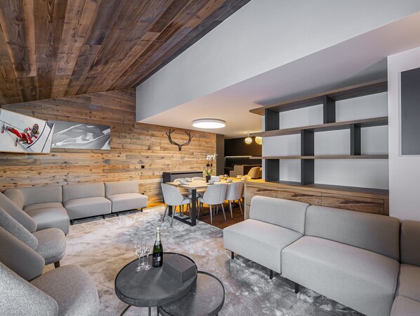 A modern living room with a wooden ceiling, a dining area with a table and chairs, and a built-in bookshelf. - Beautiful apartment in Courchevel with parking 300m from slopes (Courchevel 1550)