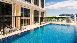 A swimming pool with lounge chairs and umbrellas, large windows, and a modern building in the background.