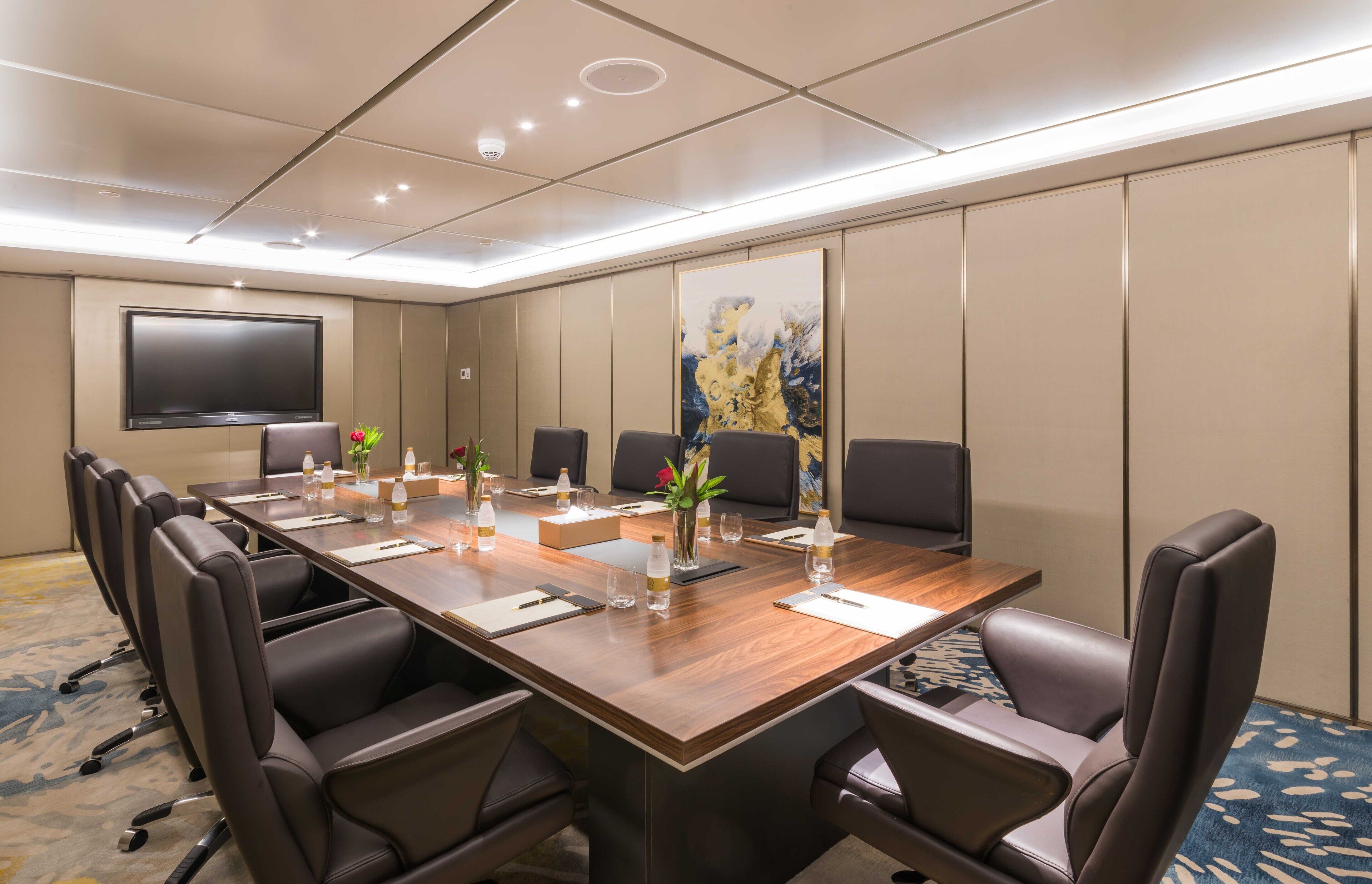 A conference room with a long table, multiple chairs, a flat-screen TV, and a large abstract painting on the wall.