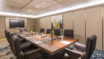 A conference room with a long table, multiple chairs, a flat-screen TV, and a large abstract painting on the wall.