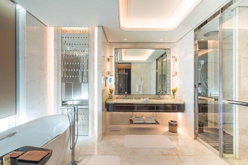 A modern bathroom with a large mirror, dual sinks, and a glass shower enclosure.