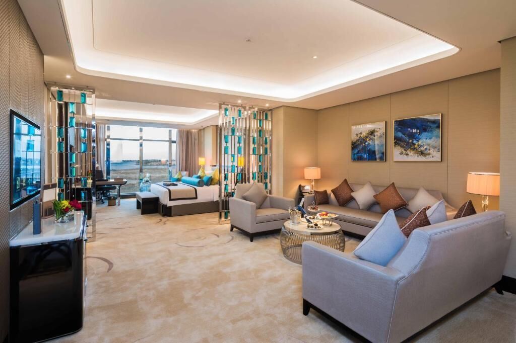Habitación de hotel moderna con sofá, sillones, televisión y vistas al exterior.