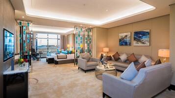 Habitación de hotel moderna con sofá, sillones, televisión y vistas al exterior.