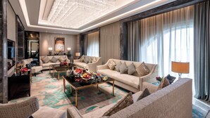 A spacious living room with a large chandelier, multiple sofas, a coffee table with decorative items, and a large window with curtains.