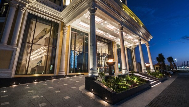 A grand hotel entrance with large columns, a well-lit facade, and a landscaped garden area.