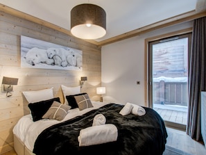 A bedroom with a large bed, wooden walls, a polar bear painting, and a balcony with a view.