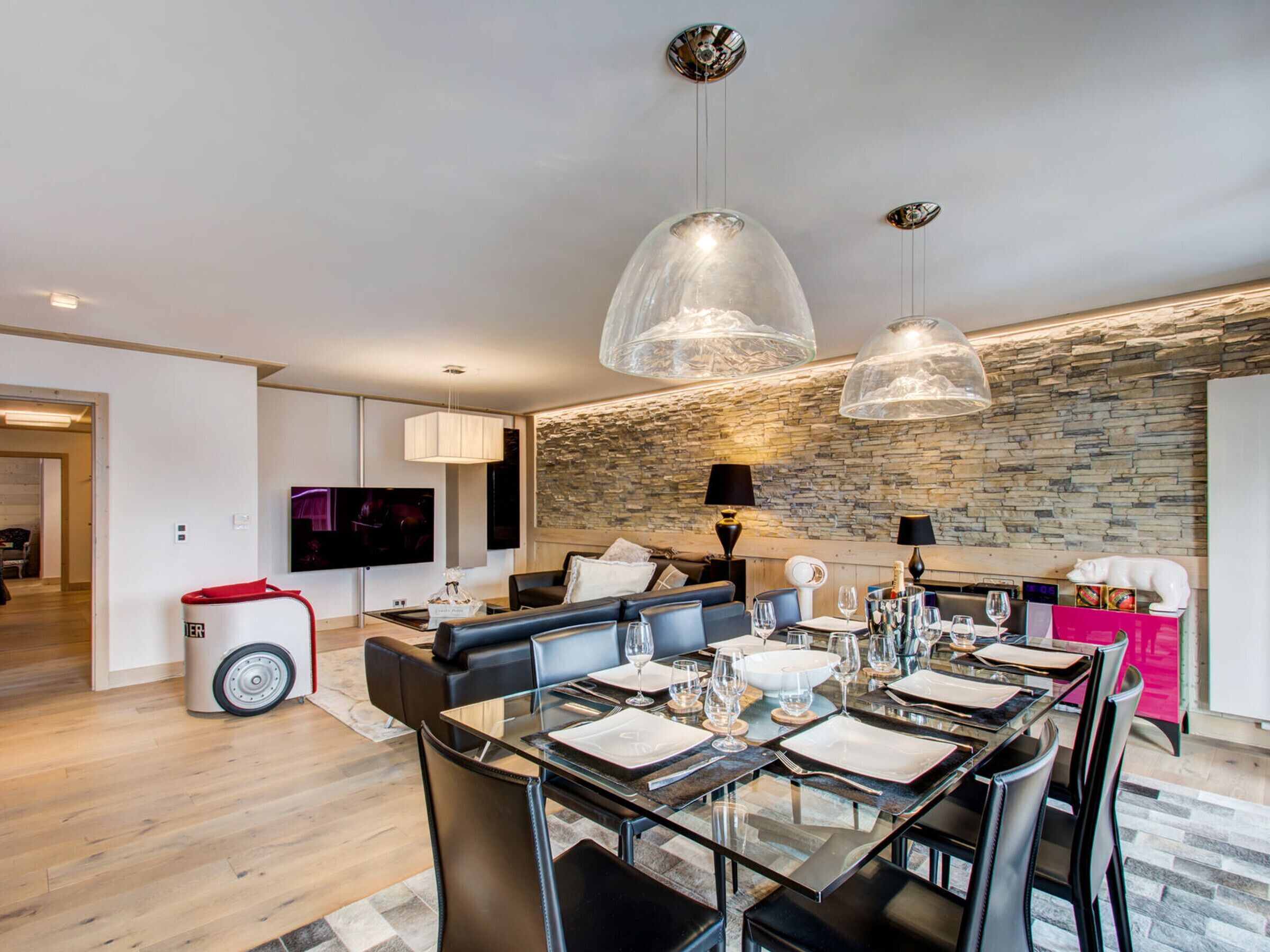 A modern living room with a stone wall, a glass dining table set for six, and a black leather sofa.