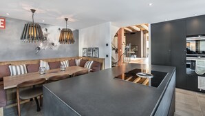 A modern kitchen with a central island, a dining area with a wooden bench, and a staircase leading to an upper level. - Modern chalet in Méribel, 5 bedrooms, jacuzzi, near cable car (Méribel)
