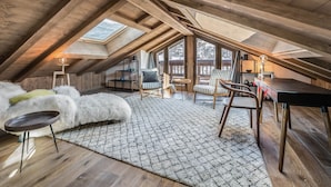 A spacious attic bedroom with a sloped ceiling, wooden beams, a skylight, a cozy seating area with a chair and a small table, and a large window offering a view of the outdoors. - Modern chalet in Méribel, 5 bedrooms, jacuzzi, near cable car (Méribel)