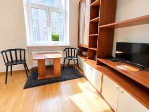 A room with a wooden desk, two chairs, a television, and a window with a view of buildings.