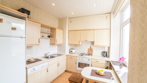 A compact kitchen with a refrigerator, stove, oven, and sink. There is a dining table with a chair and a window with a view.