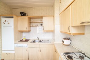 A compact kitchen with wooden cabinets, a built-in dishwasher, a sink, and a stove.