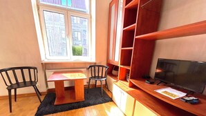 A small room with a wooden table, two chairs, a TV, and a bookshelf.