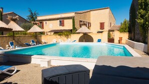 A swimming pool with lounge chairs and umbrellas, surrounded by stone buildings with red shutters.