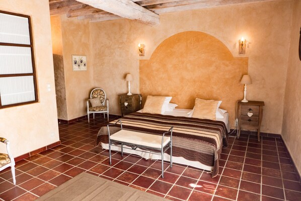 A bedroom with a bed, a nightstand, a chair, and a wall-mounted shelf.