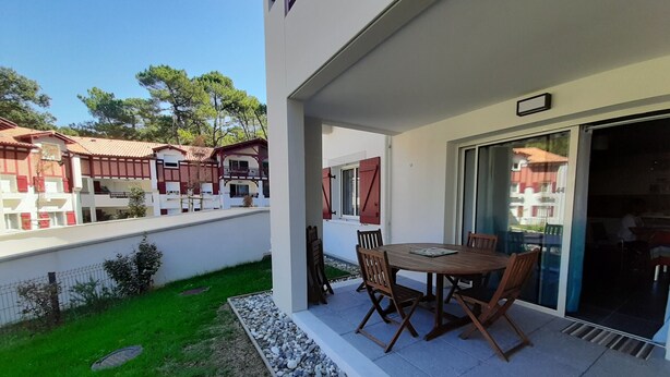 A patio with a table and chairs, a small garden area, and a view of neighboring buildings. - Lakefront Apartment with Private Garden and Secure Parking (Soorts-Hossegor)