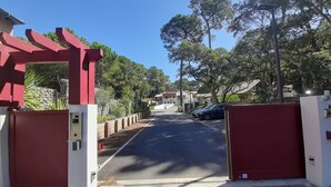 A gated driveway leading to a residential area with a stone wall and a red gate. - Lakefront Apartment with Private Garden and Secure Parking (Soorts-Hossegor)