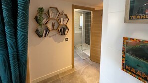 A hallway with a hexagonal bookshelf, a glass shower door, and a framed poster on the wall. - Lakefront Apartment with Private Garden and Secure Parking (Soorts-Hossegor)