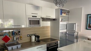 A modern kitchen with white cabinets, a microwave, a built-in oven, a coffee maker, and a refrigerator. - Lakefront Apartment with Private Garden and Secure Parking (Soorts-Hossegor)