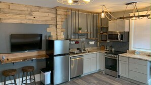 Eine moderne Küche mit Einbauofen, Mikrowelle und Edelstahlkühlschrank. Es gibt eine Holz Arbeitsplatte, ein Spülbecken und eine Theke mit Barhocker.