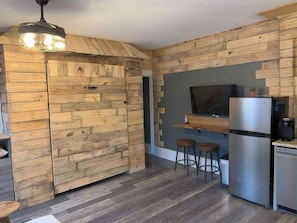 Una cocina con paredes de madera, un refrigerador de acero inoxidable y dos taburetes.