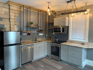 A modern kitchen with stainless steel appliances, wooden shelves, and a hanging light fixture. - Rustic 2BR Loft with River Views (Harrisburg)