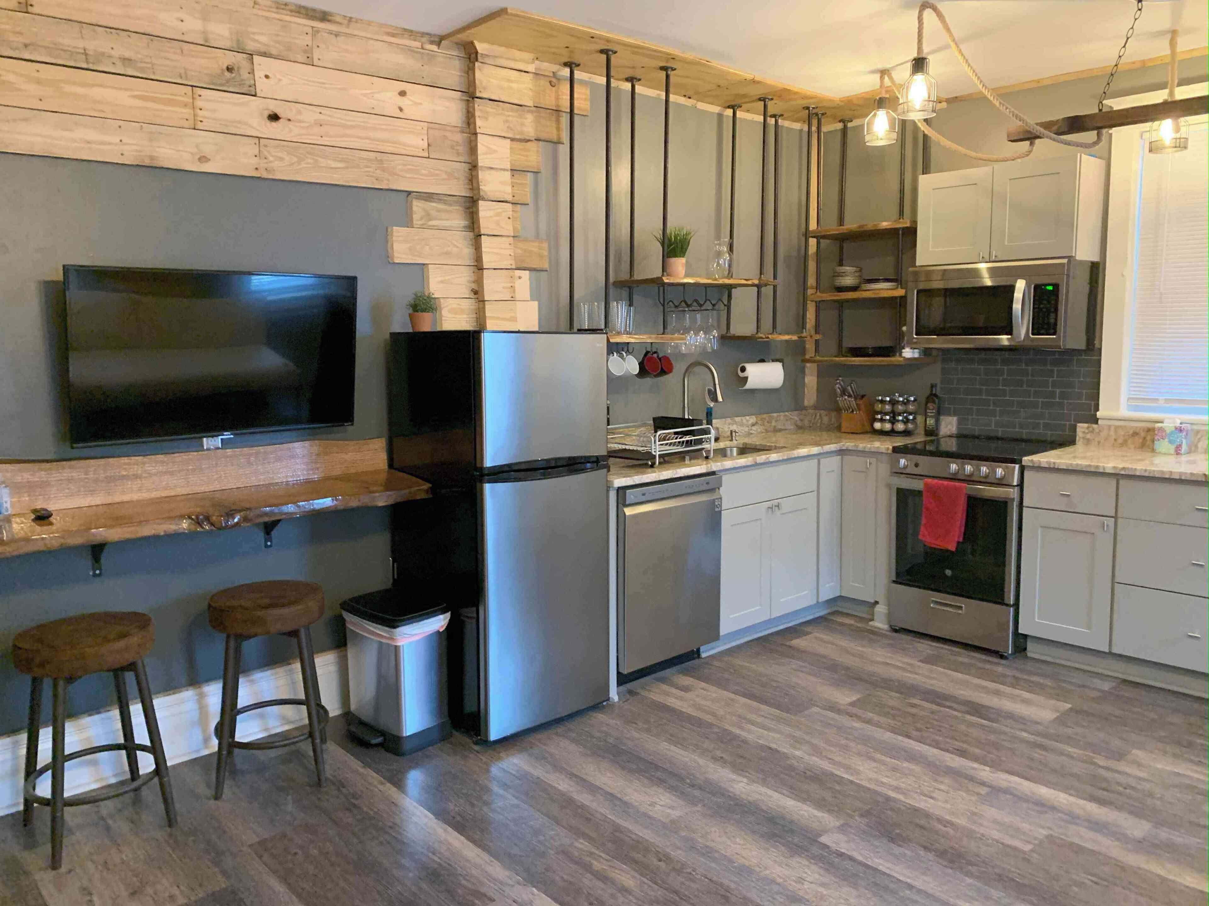 A modern kitchen with a flat-screen TV, stainless steel appliances, wooden accents, and bar stools.