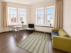 Une pièce comprenant un canapé, un téléviseur, une table avec des chaises et une fenêtre avec des rideaux.