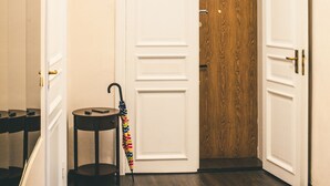 Un couloir avec une porte en bois, une petite table sur laquelle repose un parapluie et un lustre.