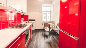 Une cuisine moderne avec des appareils électroménagers rouges, un coin repas avec des chaises et une fenêtre laissant entrer la lumière naturelle.