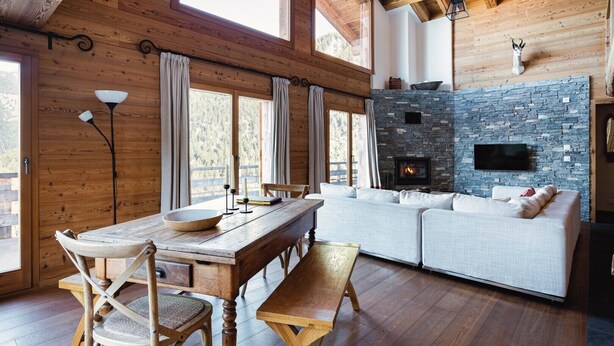 A cozy cabin interior with a stone fireplace, wooden furniture, and large windows. - Authentic Swiss Spa Chalet Hot Tub & Sauna (Riddes)