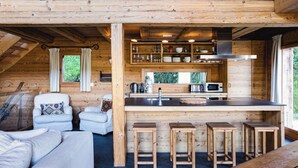 A wooden cabin with a kitchen area featuring a sink, stove, and bar stools. - Authentic Swiss Spa Chalet Hot Tub & Sauna (Riddes)